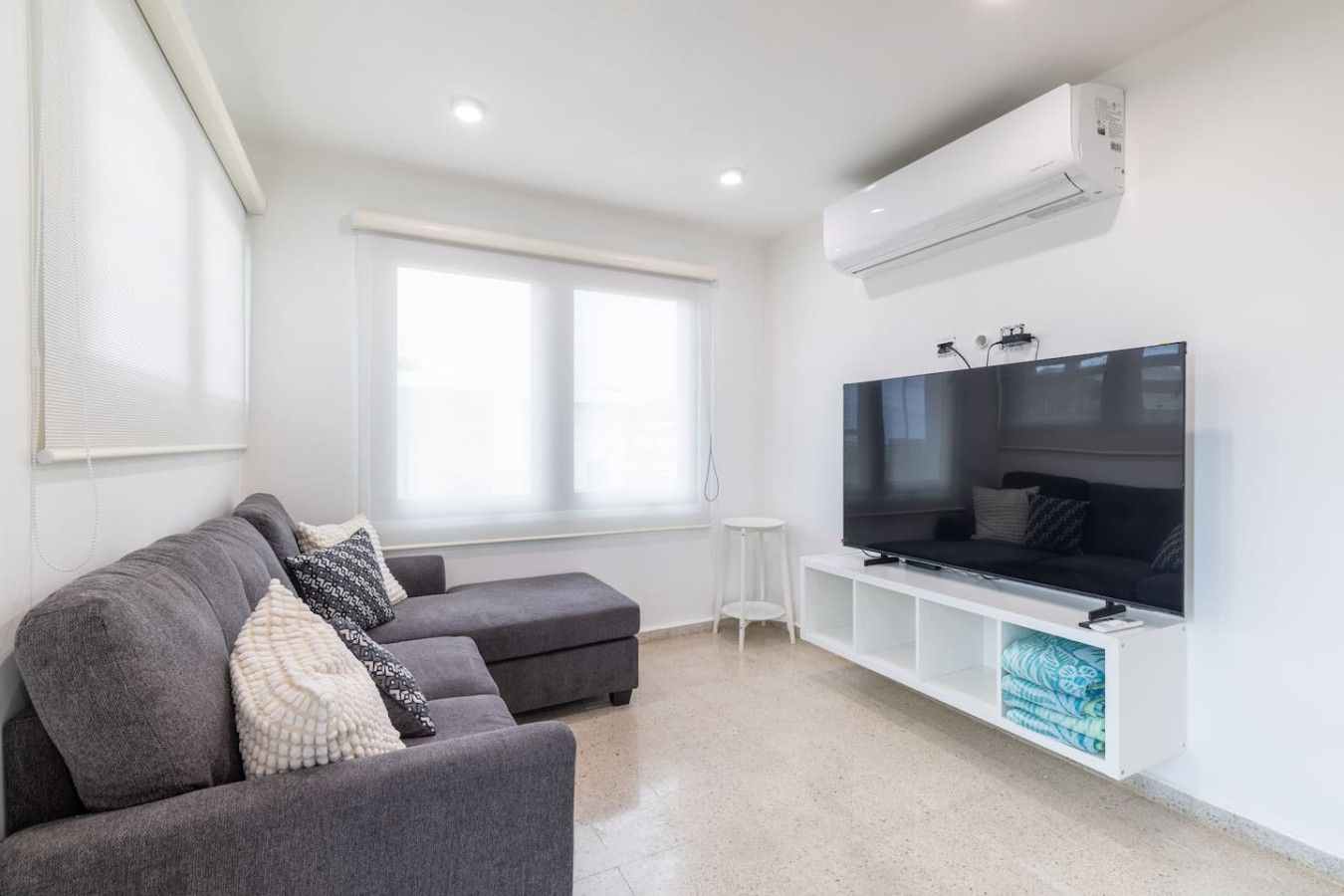 Een moderne woonkamer met een grijze bank, een flatscreen televisie en een witte televisiemeubel.