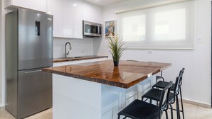 Eine moderne Küche mit einem Edelstahl-Kühlschrank, einer Mikrowelle, einer Holzinsele mit Barhocker und einem Blumentopf.
