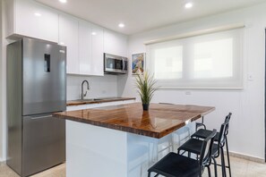 Eine moderne Küche mit einem Edelstahl-Kühlschrank, einer Mikrowelle, einer Holzinsele mit Barhocker und einem Blumentopf.