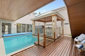 A swimming pool with a wooden deck, a covered seating area, and a view of the surrounding buildings. - The Rise | Pool, Playroom & Sauna near Hillarys (Hillarys)