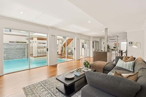 Ein großzügiger Wohnraum mit einem grauen Sofa, einem Couchtisch und Blick auf einen Swimmingpool durch Glastüren.