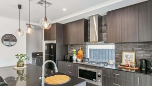 Une cuisine moderne avec des meubles de couleur bois foncé, un îlot central doté d’un évier et des luminaires suspendus.