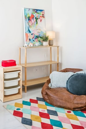 Une pièce avec une étagère en bois, un tapis coloré, un canapé en cuir marron et un tableau accroché au mur.