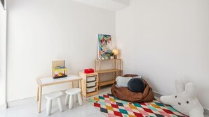 Une salle de jeux pour enfants avec un bureau, des tabourets, un fauteuil poire et un tapis coloré.