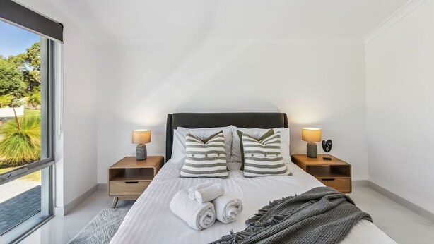 Une chambre moderne avec un grand lit, deux tables de chevet avec des lampes, une vue sur la verdure et une porte-fenêtre coulissante.
