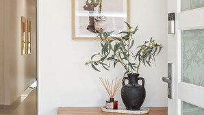 Ein Flur mit einem Holzkonsolentisch, einer schwarzen Vase mit Pflanze, einem gerahmten Bild und einem Korbwäscher.