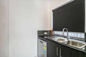 A modern kitchen with a black countertop, stainless steel sink, and a dishwasher. - The Rumpus House | 5BR + Playroom near City Beach (Wembley Downs)