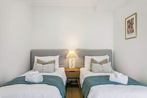 A hotel room with two beds, a nightstand with a lamp, and a framed picture on the wall. - Kids Play Room | 75 Inch TV | WFH Space (Wembley Downs)