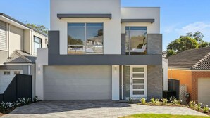 Une maison moderne à deux étages, dotée d’un garage, de grandes fenêtres et d’une pelouse bien entretenue.
