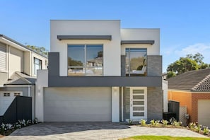 Une maison moderne à deux étages, dotée d’un garage, de grandes fenêtres et d’une pelouse bien entretenue.
