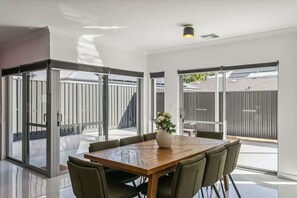 A modern dining area with a wooden table, green upholstered chairs, and a vase of flowers. - The Rumpus House | 5BR + Playroom near City Beach (Wembley Downs)