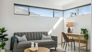 Un salon moderne avec un canapé gris, une table basse ronde en bois, un bureau avec une chaise et une grande fenêtre.