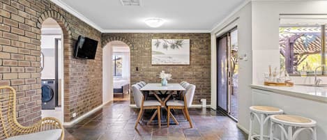 A dining area with a brick wall, a television mounted above a washing machine, and a view of the outdoors through a door.