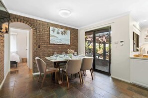 Comedor con pared de ladrillo, una mesa dispuesta para cuatro personas y vista a través de un ventanal.
