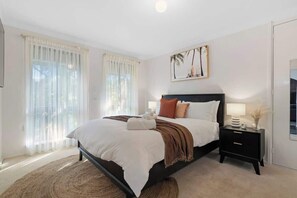 Un dormitorio con cama, cortinas, mesita de noche y una obra de arte colgada en la pared.