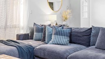 A living room with a grey sofa, a wooden coffee table, a ceiling fan, and a large window with sheer curtains.