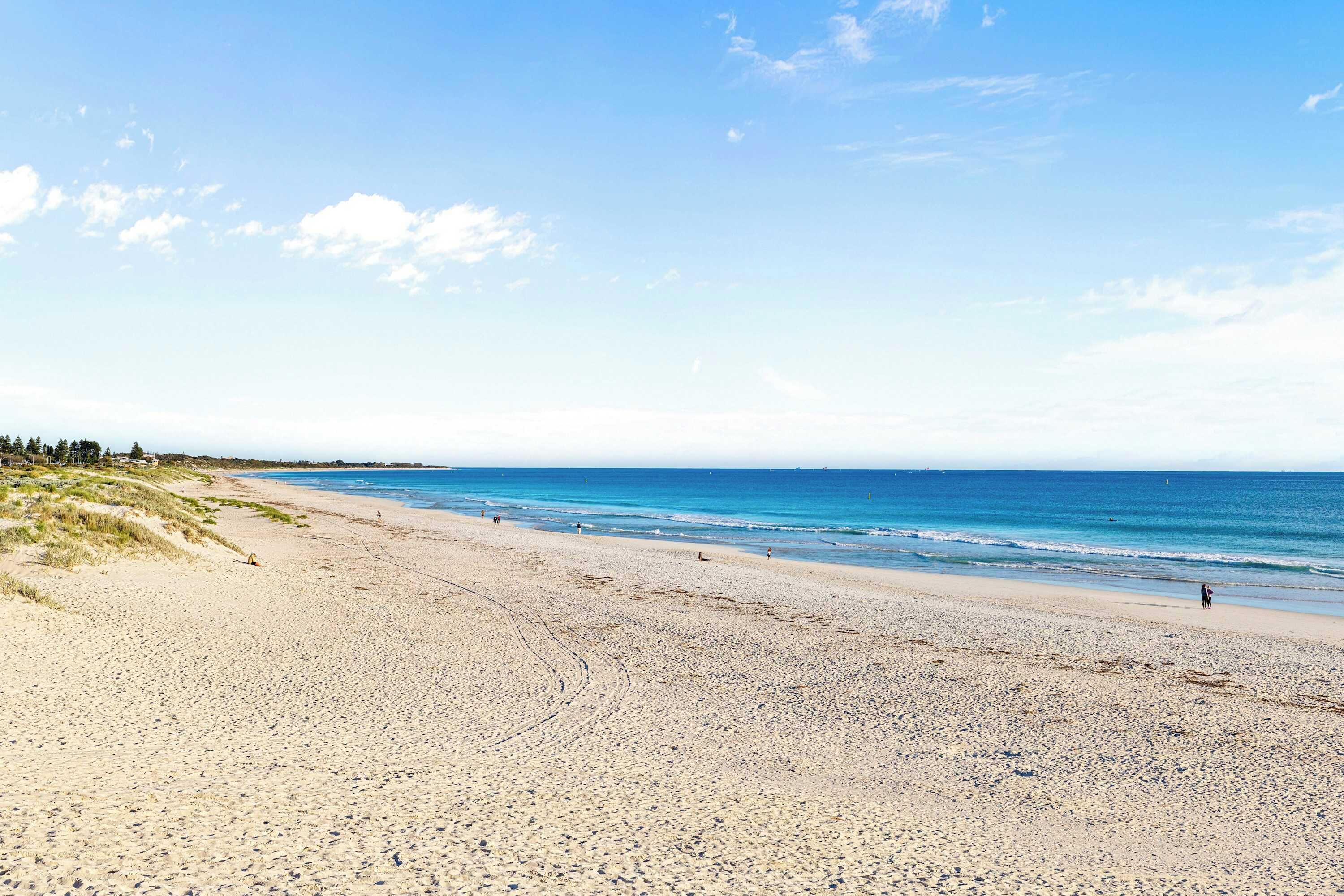 A beach with a clear sky, calm sea, and a few people walking.