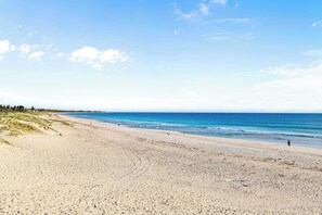 Una playa con cielo despejado, mar tranquilo y algunas personas caminando.
