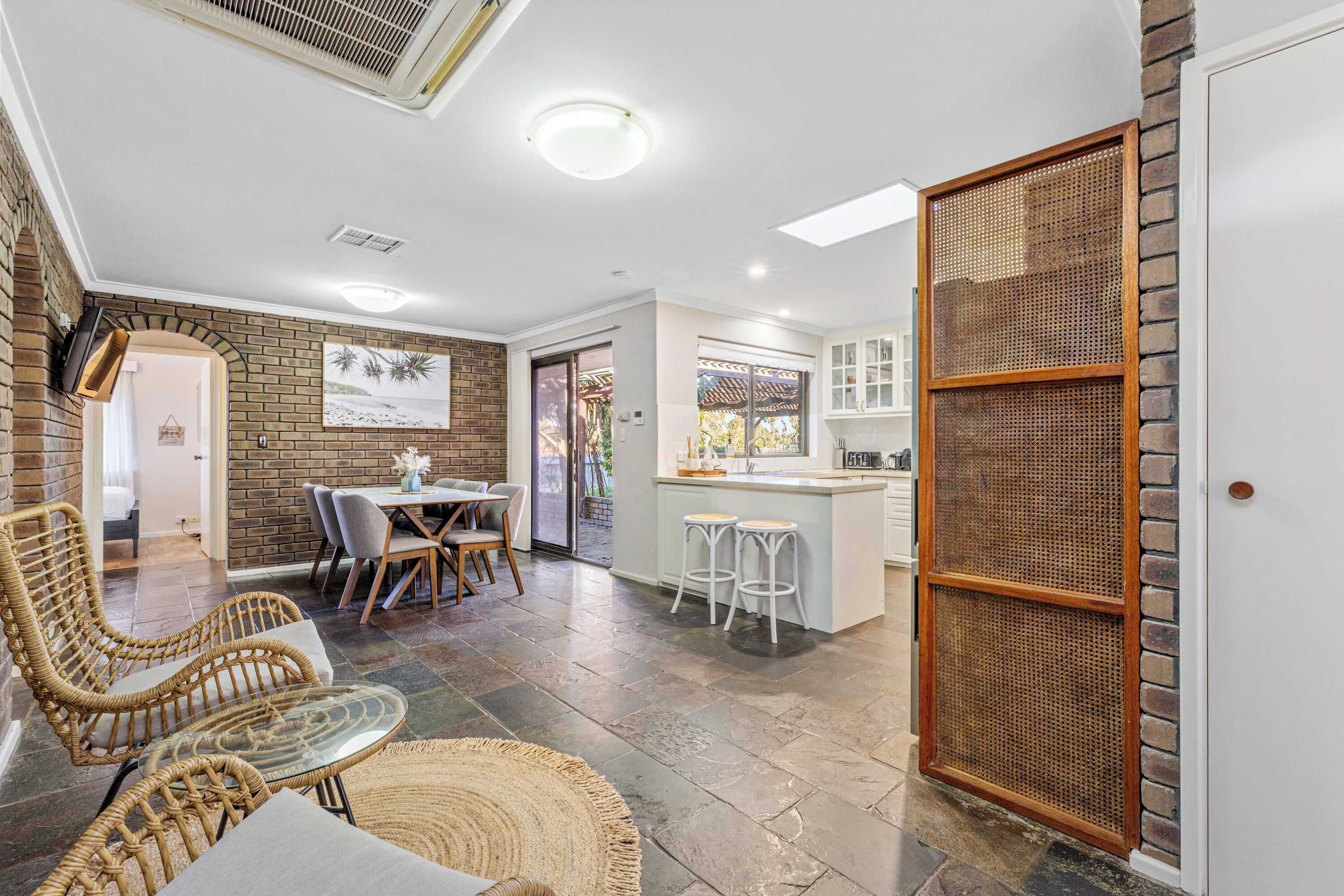 A modern kitchen with white cabinets, a dining area with wicker furniture, and a view of the outdoors.