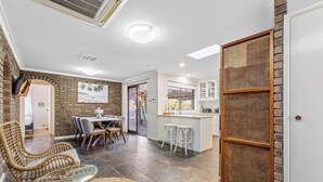 Una cocina moderna con armarios blancos, un comedor con mobiliario de mimbre y vistas al exterior.