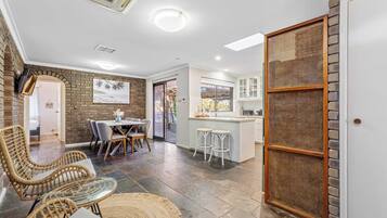 A modern kitchen with white cabinets, a dining area with wicker furniture, and a view of the outdoors.