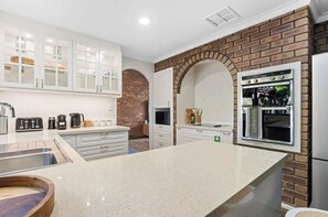 Una cocina moderna con muebles blancos, una pared de ladrillo decorativa, horno empotrado y una isla grande con lavamanos.