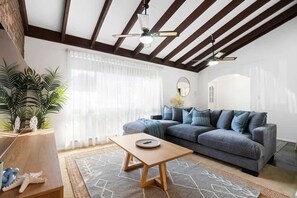 Una sala de estar con sofá, una mesa de centro, un ventilador de techo y un ventanal con cortinas.