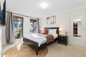 A bedroom with a bed, bedside tables, a TV, and a window with curtains.