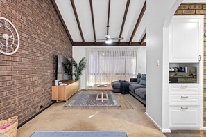 A living room with a brick wall, a ceiling fan, a sofa, a coffee table, and a cabinet.
