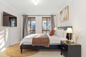 Un dormitorio con cama, mesita de noche, lámpara y una obra de arte.