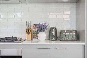 A kitchen with a gas stove, a toaster, a set of knives, a book, and a vase with flowers.