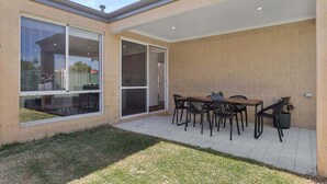 A patio with a table and chairs, a sliding glass door, and a brick wall. - The Tobias | 4BR, Park-Front + Double Garage (Bayswater)