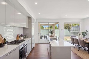 Une cuisine moderne avec des meubles blancs, un îlot central et un coin repas donnant sur le jardin.