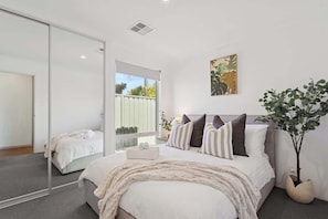 Une chambre à coucher avec un lit, un miroir, une fenêtre et une plante.