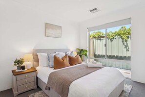 A bedroom with a bed, bedside table, lamp, and a view of greenery outside.