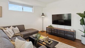 A modern living room with a sofa, coffee table, TV, and a plant. - The Tobias | 4BR, Park-Front + Double Garage (Bayswater)