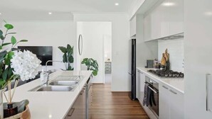 A modern kitchen with white cabinetry, stainless steel appliances, and a wooden floor. - The Tobias | 4BR, Park-Front + Double Garage (Bayswater)