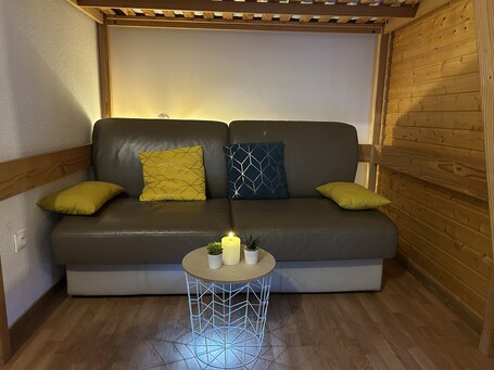 A cozy room with a sofa, cushions, a small round table with a candle, and a potted plant.. Apartment 'Orelle Spa Et Piscine' with Wi-Fi