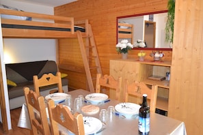 Una cama literera con escalera, sillas de madera, una mesa de comedor con platos, vasos y una botella.