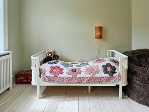 En hvid tremmeseng med et blomstret tæppe, en bamse og en lampe på væggen.