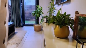 Ein modernes Wohnzimmer mit Fernseher, Topfpflanzen, einer Uhr und einer Glasschiebetür, die auf einen Balkon führt.
