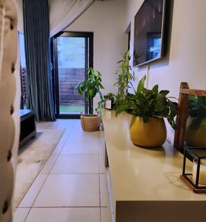 Ein modernes Wohnzimmer mit Fernseher, Topfpflanzen, einer Uhr und einer Glasschiebetür, die auf einen Balkon führt.