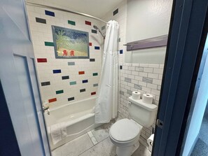 Kylpyhuone, jossa on suihku, wc ja seinälle kiinnitetty hylly, jossa on kaksi rullaa wc-paperia.