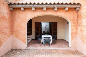 Un patio al aire libre con una mesa y sillas, un arco y vistas a una habitación con una puerta y una ventana.