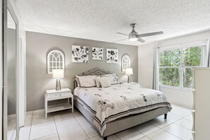 Ein Schlafzimmer mit einem Bett, Nachttischen, Wandbildern, einem Deckenventilator und einem Fenster.