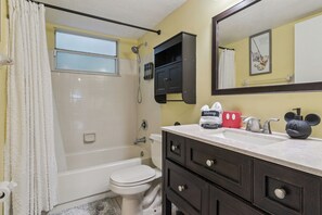 Ein Badezimmer mit Badewanne, Toilette, Schminktisch mit Schubladen, einem Spiegel und einer Mickey Mouse Figur.