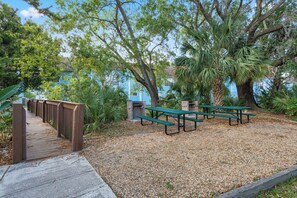Una terraza de madera que lleva a un área de picnic con bancos y un árbol.