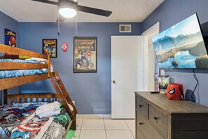 Una habitación con literas, ventilador de techo, un cartel de Capitán América, televisor y cómoda.