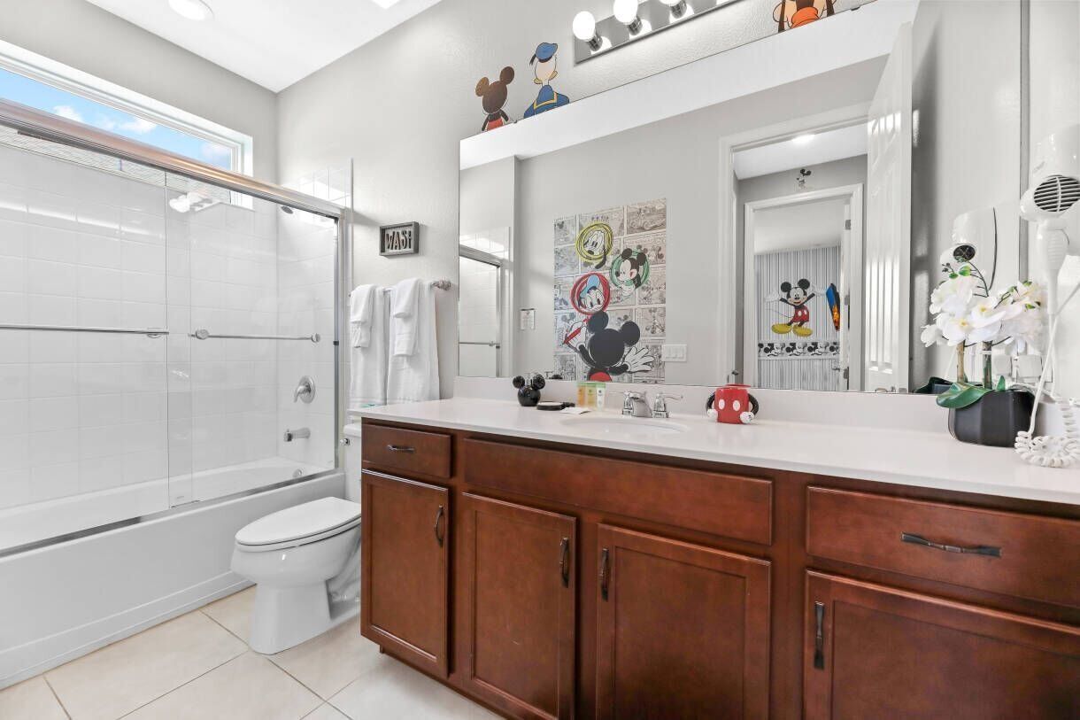 A modern bathroom with a glass shower, a white toilet, wooden cabinets, and a large mirror with cartoon character decorations.