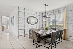 Ein Essbereich mit Wand im Marmor-Design, einem runden Spiegel, einer Kandelaber und Blick durch große Fenster.